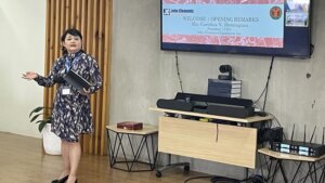 female speaker presenting with TV in background 