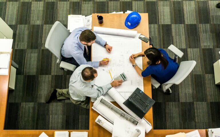 three people sitting around a table while looking over some paper