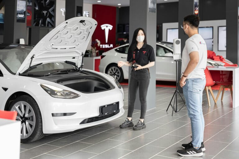 woman selling white tesla car to man in showroom