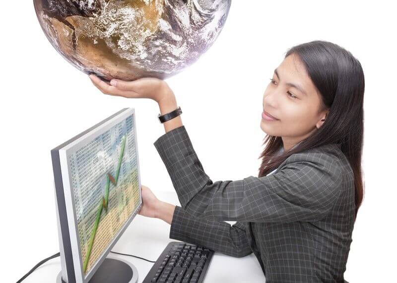 Businesswoman holding a globe while sitting at a desk with a computer displaying a growth chart, symbolizing global outsourced staffing trends.