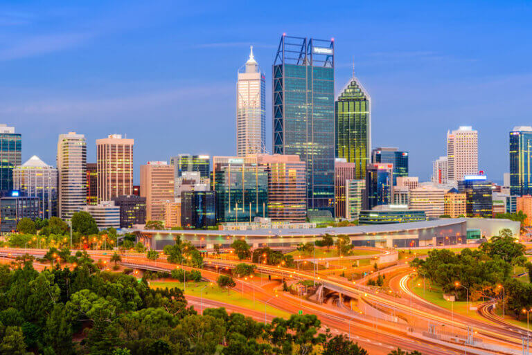 A vibrant skyline of a modern city with tall buildings and lush greenery surrounding illuminated highways at dusk. This image showcases the concept of sustainable livable cities, blending urban development with green spaces to promote economic growth and quality of life.