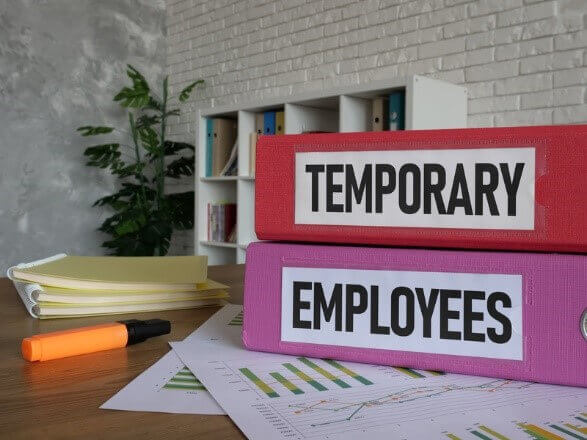 Binders labeled 'Temporary Employees' on a desk with documents, highlighting the use of volume staffing for workforce management.