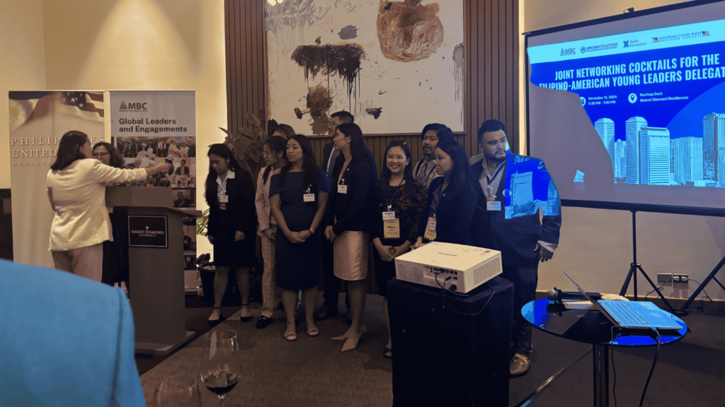 Filipino-American young professionals standing together at the Joint Networking Cocktails event, with a presenter at the podium and banners in the background highlighting global engagement.