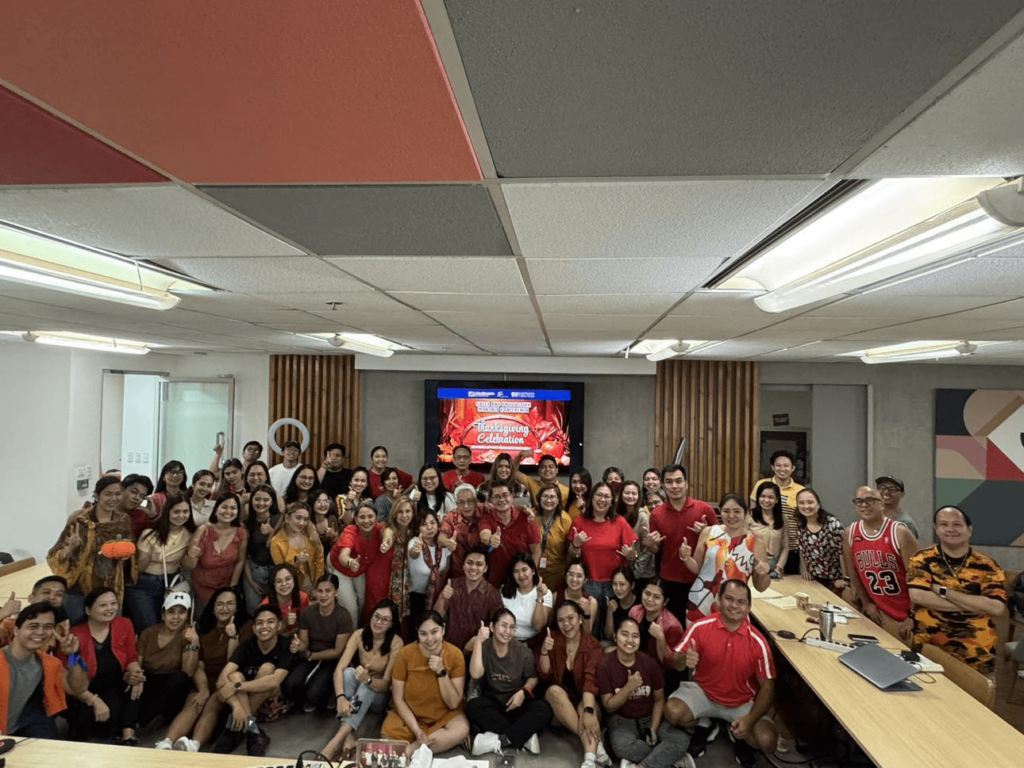 Employees gathered in a brightly lit conference room, smiling and posing for a group photo during a Thanksgiving celebration, embodying gratitude in the workplace.