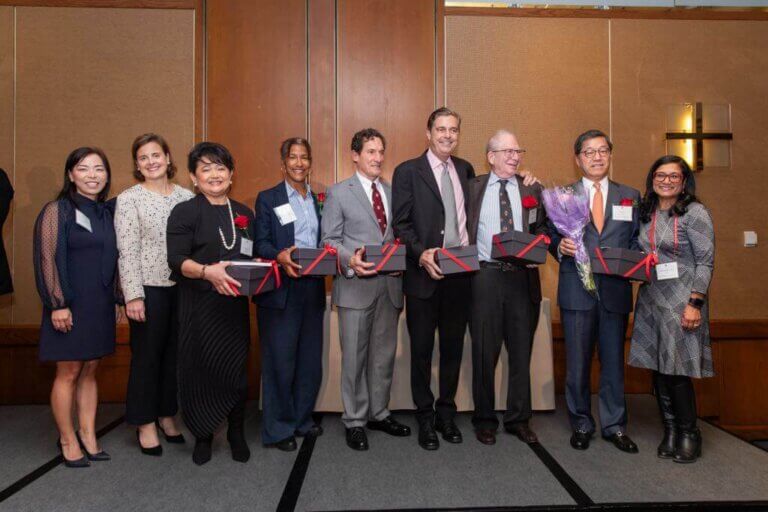 Group of individuals posing on stage holding awards, representing the recipients of the Harvard Alumni Award.