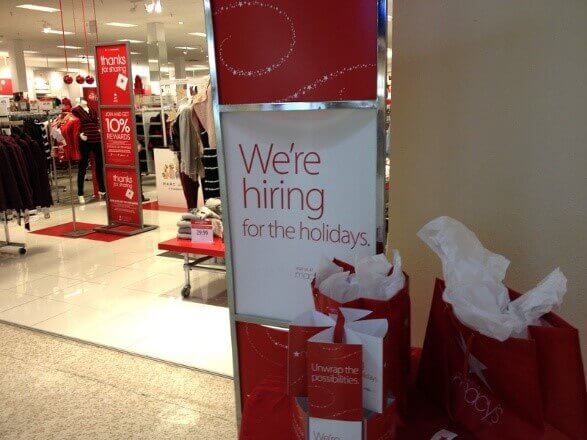 Store holiday hiring sign with red gift bags, representing tips for balancing job search and holiday stress during the festive season.