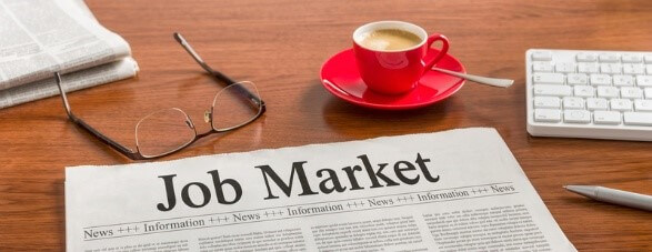 Newspaper on a desk with the headline 'Job Market,' next to glasses, a coffee cup, and a keyboard, representing 2025 job market trends.