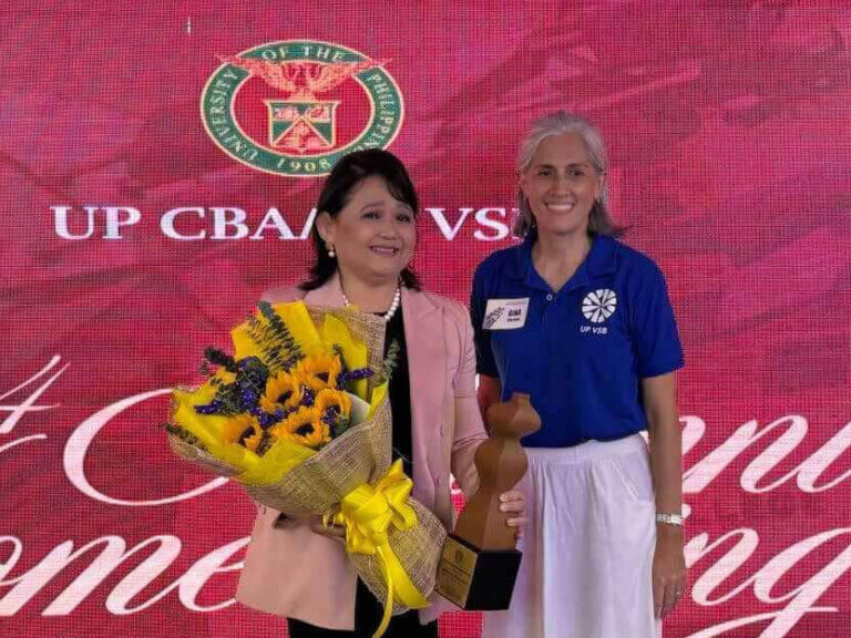 Carol Dominguez receives the Distinguished Alumnus Award, holding a bouquet and trophy, alongside a representative from the UP Virata School of Business.