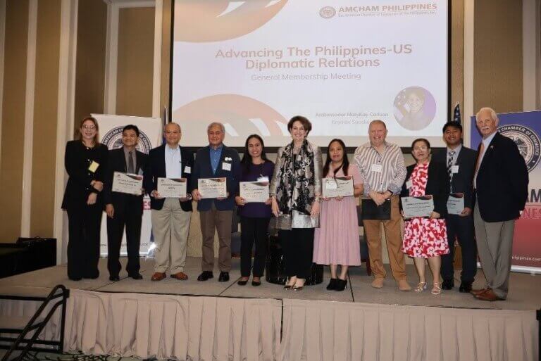 Attendees at the AmCham Philippines event on US-Philippine Partnership 2024, holding certificates in front of a presentation screen.