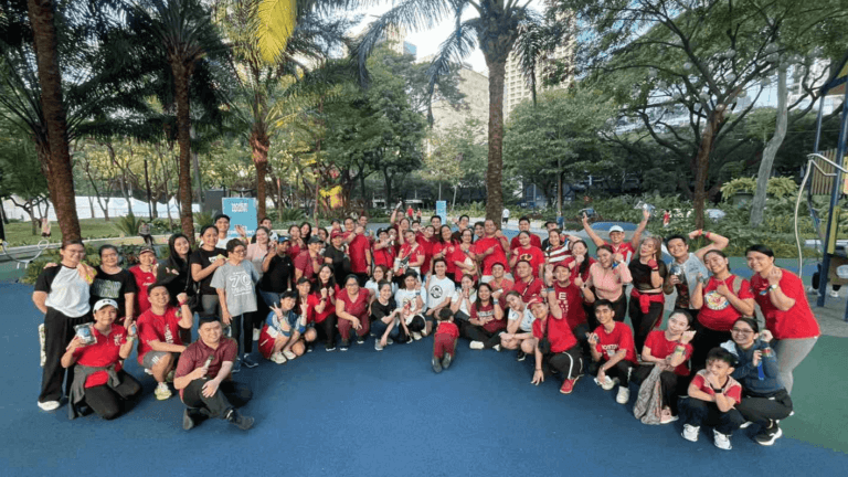 A large group of employees in red and athletic wear gathers at a park, celebrating a corporate fun run with smiles and energetic poses.