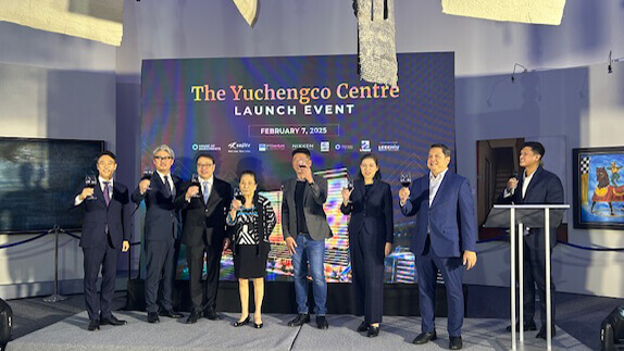 A group of people stand on a stage at the Yuchengco Centre Makati launch event, holding glasses. A large screen behind them displays event details, dated February 7, 2025.