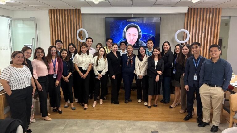 Participants of a learning session on customer-centric strategy pose for a group photo in an office setting, with a virtual attendee joining on-screen.