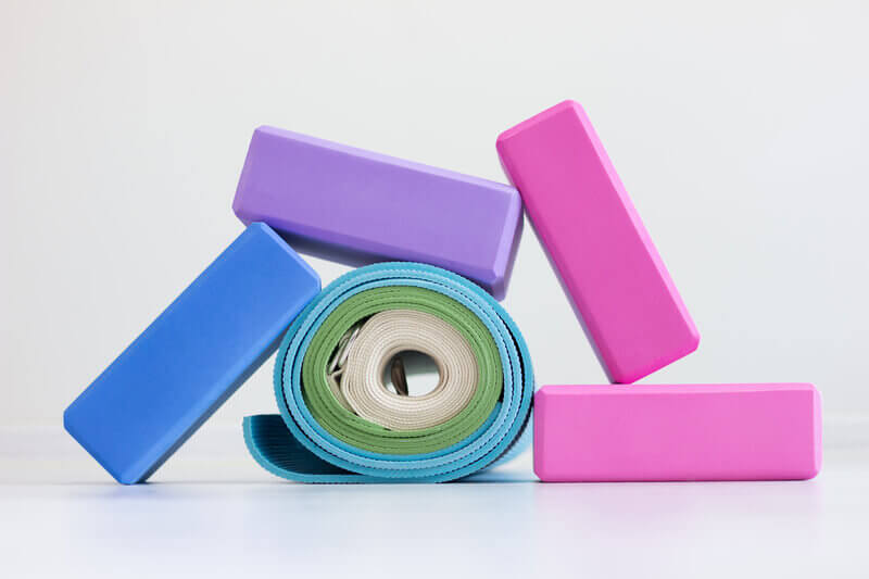 Stacked yoga blocks and rolled-up straps used in Iyengar yoga, promoting workplace wellness through alignment and support.