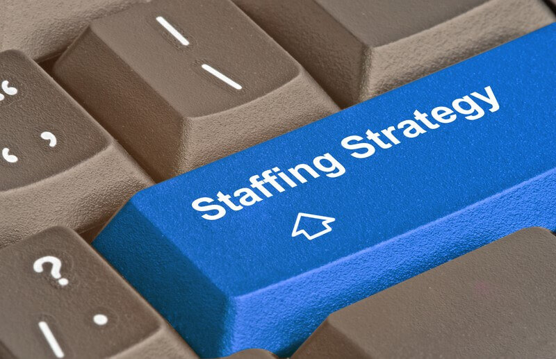 A keyboard with a blue key labeled "Staffing Strategy," symbolizing the choice between outsourced staffing vs. in-house hiring.