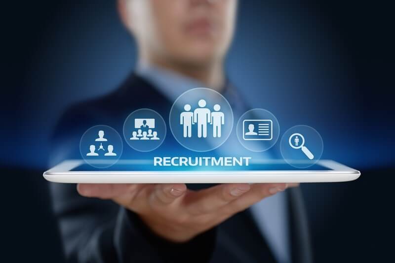 A businessman holds a digital tablet displaying icons related to recruitment, symbolizing the best tools for recruiters in a tech-driven hiring process.