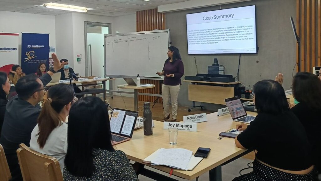 Participants engage in a workshop on effective team leadership, discussing a case study in a classroom setting with a presenter facilitating.