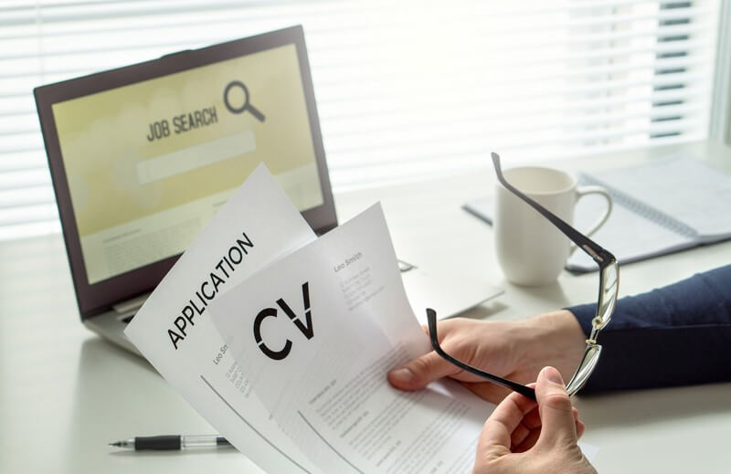Person reviewing a CV and job application in front of a laptop displaying a "Job Search" screen, representing modern job search strategies using both digital tools and traditional documents. Would you like a more SEO-optimized version as well?
