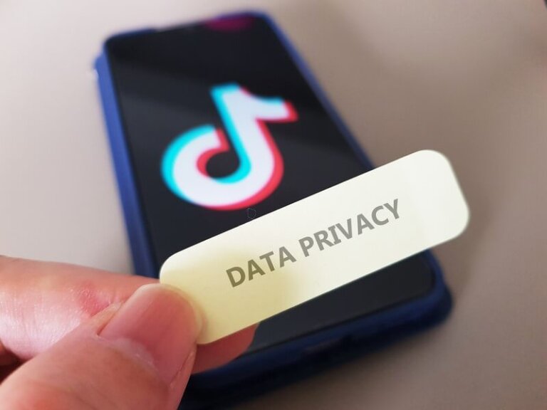 A smartphone displaying the TikTok logo on its screen with a hand holding a label that says "DATA PRIVACY," symbolizing concerns over TikTok data privacy and security.
