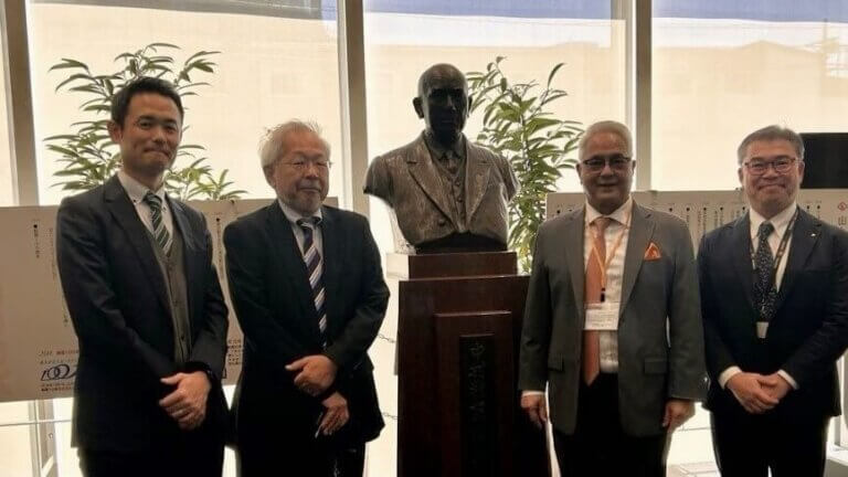 Four professionals pose beside a statue during a business trip to Japan for client engagement, highlighting cross-cultural partnership and collaboration.