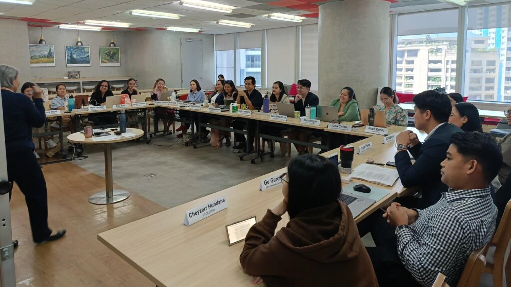 A diverse group of professionals engages in an interactive workshop on effective networking, seated in a U-shaped setup with nameplates, laptops, and notebooks.