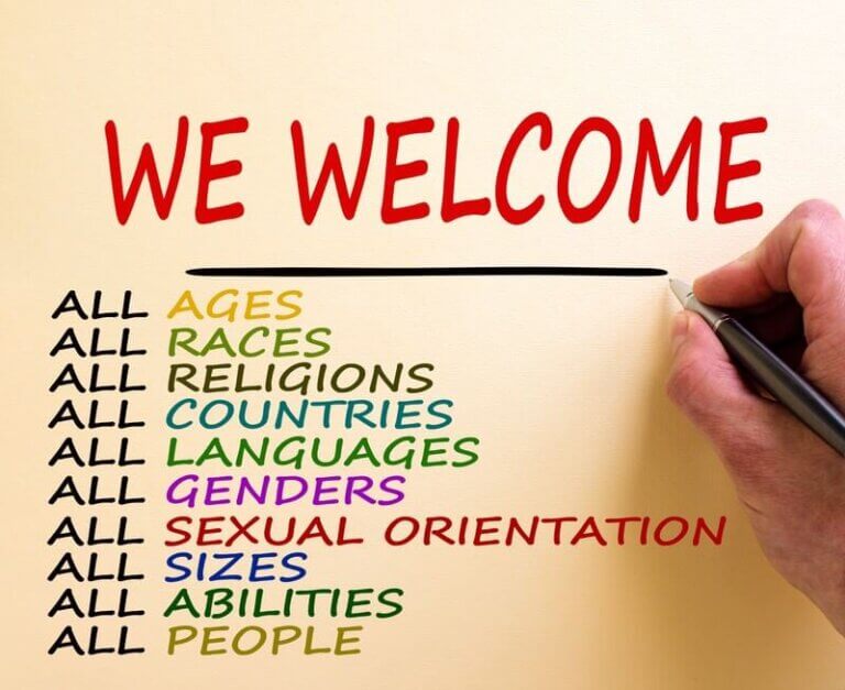 A hand writing on a poster that reads “We Welcome All” followed by a list of groups, promoting diversity and inclusive leadership.