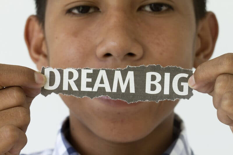 A young Filipino holds a torn paper strip with the words "DREAM BIG," symbolizing ambition and hope tied to The Filipino Dream.