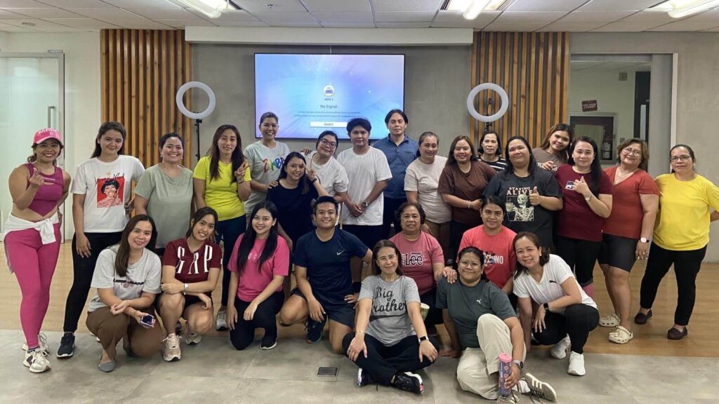 A group of employees poses together in a brightly lit office space after a fitness session, showcasing participation in workplace wellness programs.