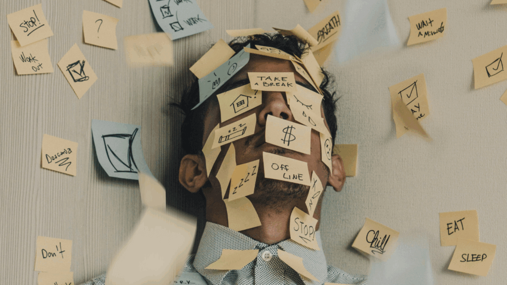 Person overwhelmed by sticky notes with reminders like 'CHILL,' 'DEADLINE,' and 'TAKE A BREAK'—visually representing stress and mental clutter.